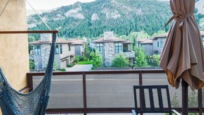 A balcony with a hammock and a chair, overlooking a row of stone buildings with a mountainous backdrop.