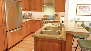 A kitchen with wooden cabinets, a stainless steel refrigerator, a stove, and a sink.