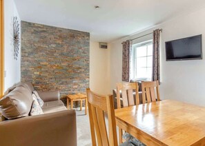 A living room with a stone wall, a sofa, a dining table with chairs, and a TV mounted on the wall.