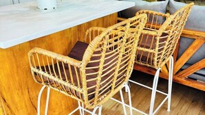 Un coin cuisine avec un comptoir en bois, deux tabourets de bar en osier dotés de coussins, un four à micro-ondes et une plante en pot.