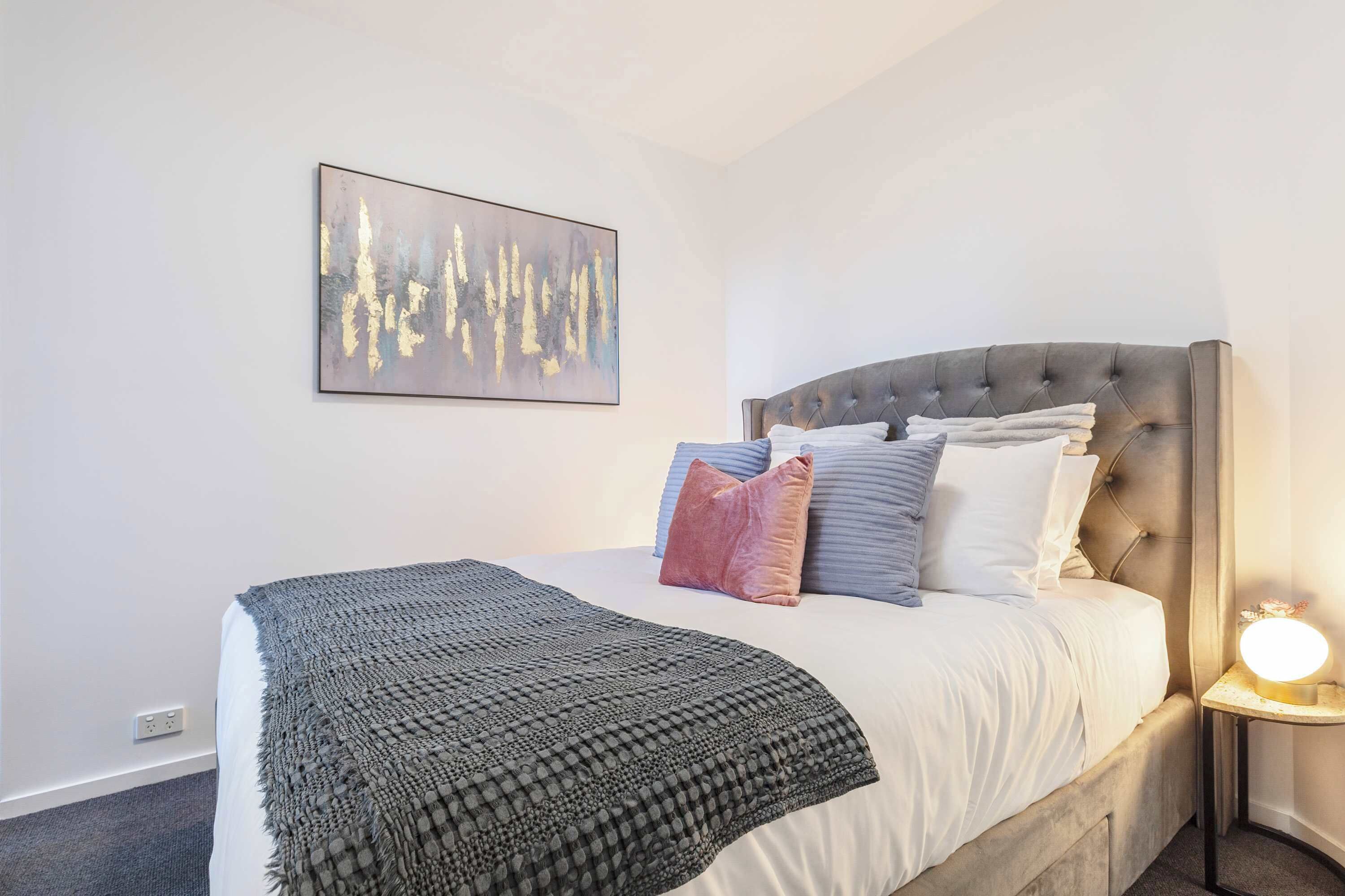 Ein Schlafzimmer mit Bett, Kissen, Decke, Wandbild und Nachttischlampe.