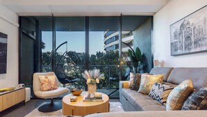 A modern living room with a sofa, armchair, coffee table, and a large window offering a view of buildings and trees.