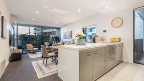 A modern kitchen with a central island, a dining area with a sofa and chairs, and large windows offering a view of the outside.
