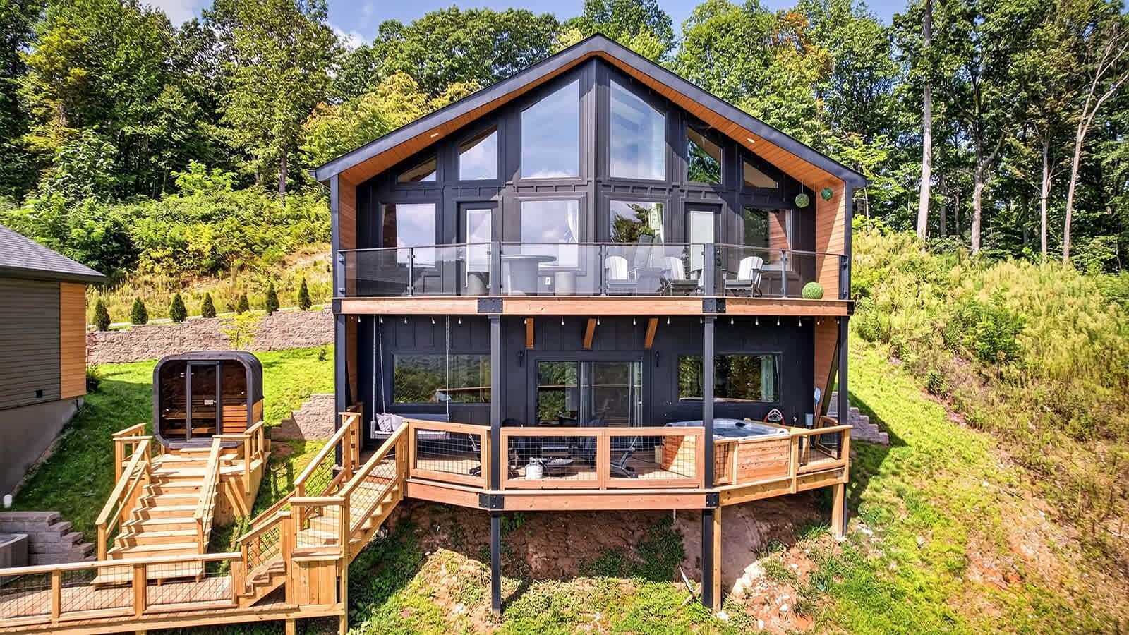 A two-story wooden cabin with a balcony, a hot tub, and a sauna.