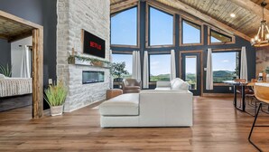 A spacious living room with a stone wall, a fireplace, a large window, and a cozy seating area.