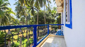 Un balcon doté d’une balustrade bleue, donnant sur un jardin planté de palmiers.