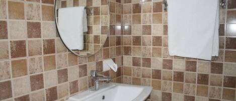 A bathroom with a white sink, a round mirror, and two white towels hanging on the wall.