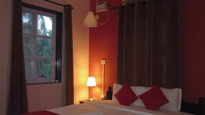 Une chambre d’hôtel équipée d’un lit, d’un ventilateur de plafond, d’un climatiseur, d’une fenêtre avec des rideaux et d’une table de chevet avec une lampe.