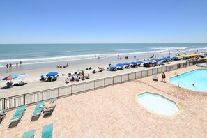 A beach view with a pool area, sun loungers, and umbrellas.