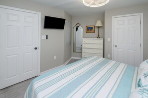 Une chambre à coucher avec un lit, une commode, une télévision et un miroir.