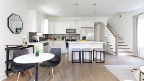 A modern kitchen with white cabinets, a central island, and a dining area with black chairs and a white table.