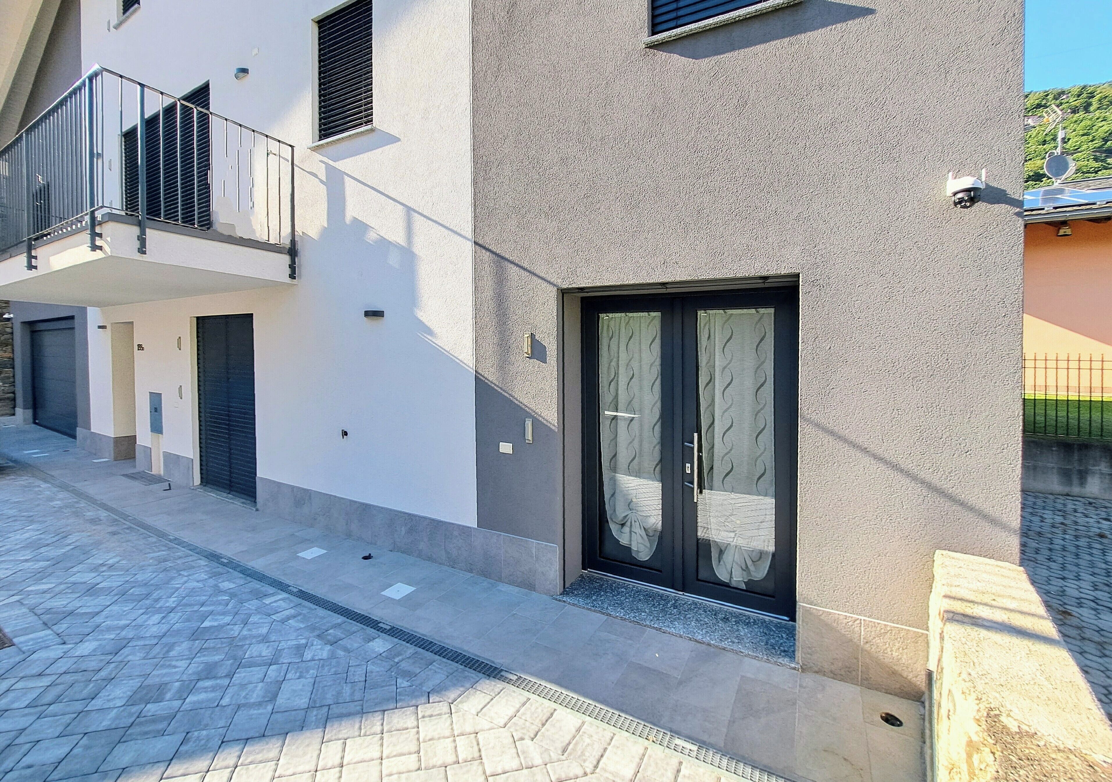 Un bâtiment moderne doté d’un balcon, d’une porte avec un rideau et d’une caméra de surveillance.