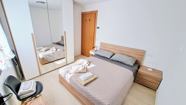 A modern hotel room with a large bed, a wooden headboard, a bedside table, a chair, and a mirror. - Cozy lodging between the lake and the mountains (Morbegno)