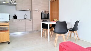 A modern kitchen with light wood cabinets, a white countertop, and a built-in oven. There is a dining area with a white table and black chairs. - Cozy lodging between the lake and the mountains (Morbegno)
