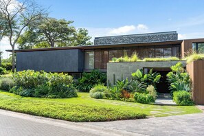 A modern building with a flat roof, stone facade, and a garden with various plants and a stone pathway. - 6 BR Architectural Masterpiece in Peninsula Papagayo (Nacascolo)