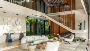 A modern living room with a white sofa, a coffee table, and a white armchair. There is a staircase with glass railings leading to an upper level. - 6 BR Architectural Masterpiece in Peninsula Papagayo (Nacascolo)