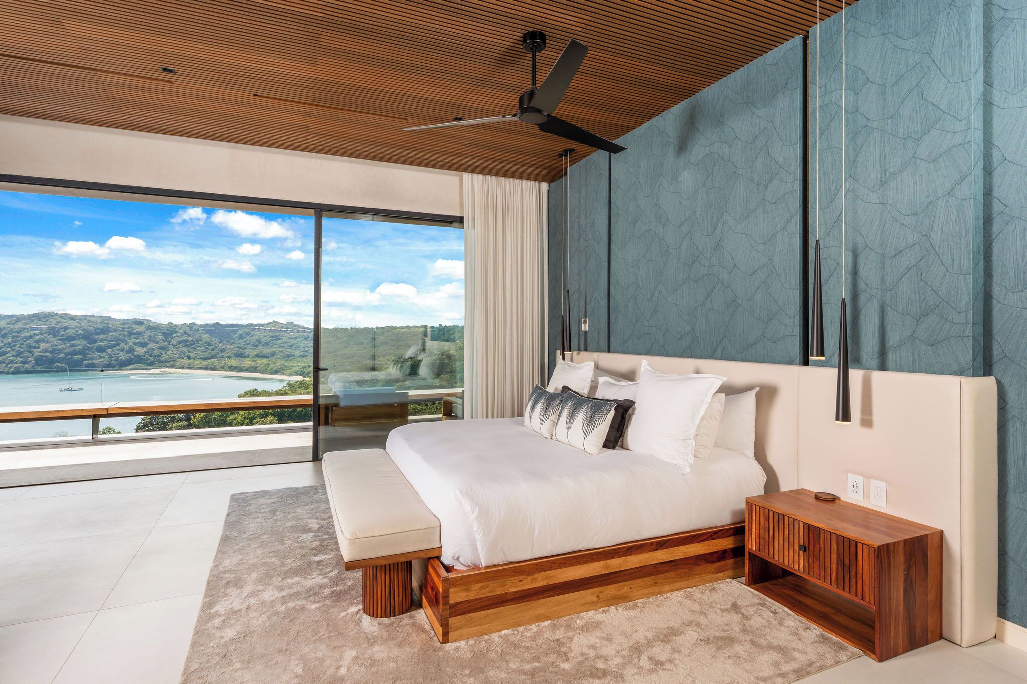 Un dormitorio moderno con una cama grande, cabecera de madera y vistas a la playa.