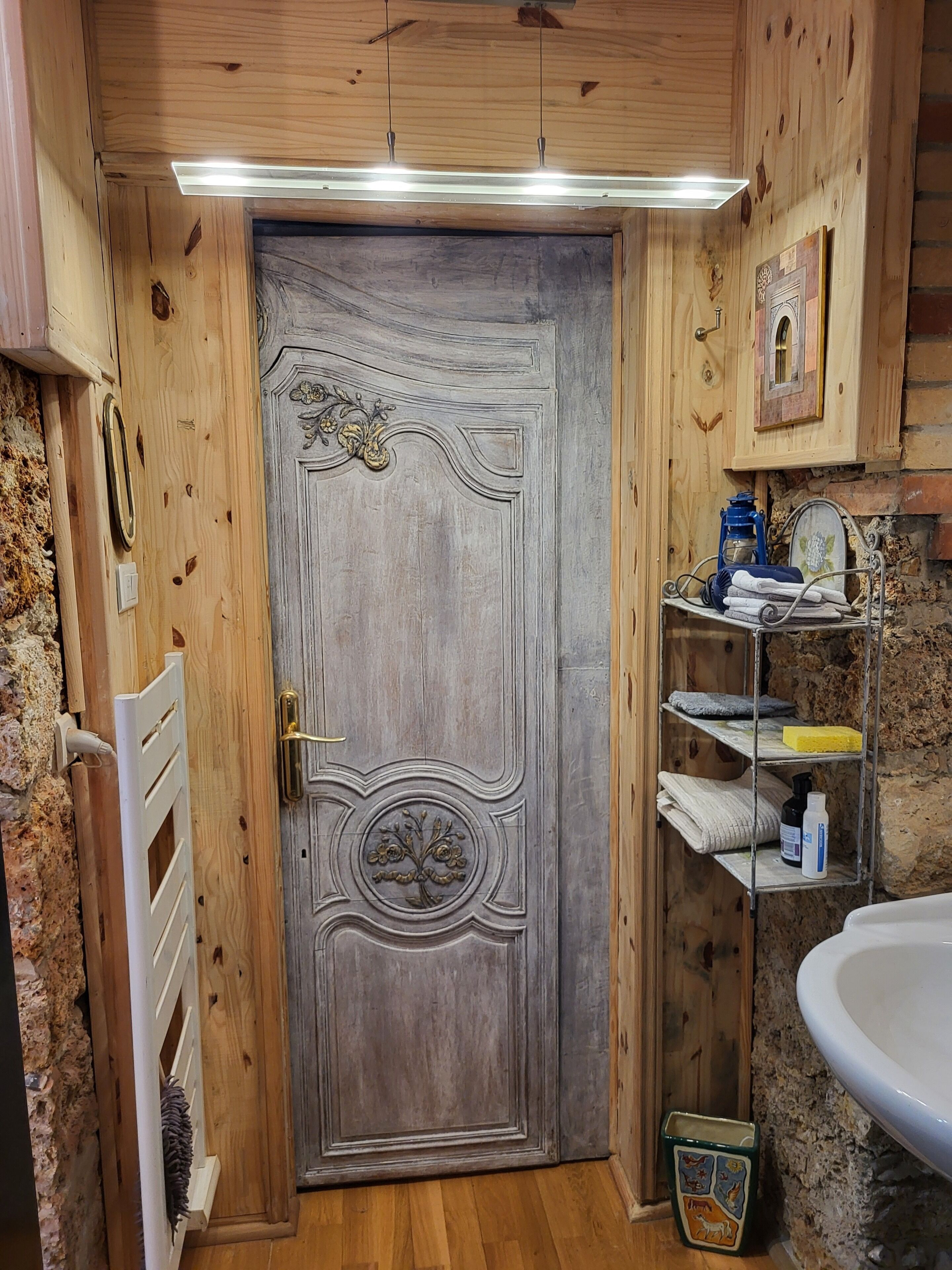 A wooden door with intricate carvings, a metal shelf with towels and toiletries, and a white sink.