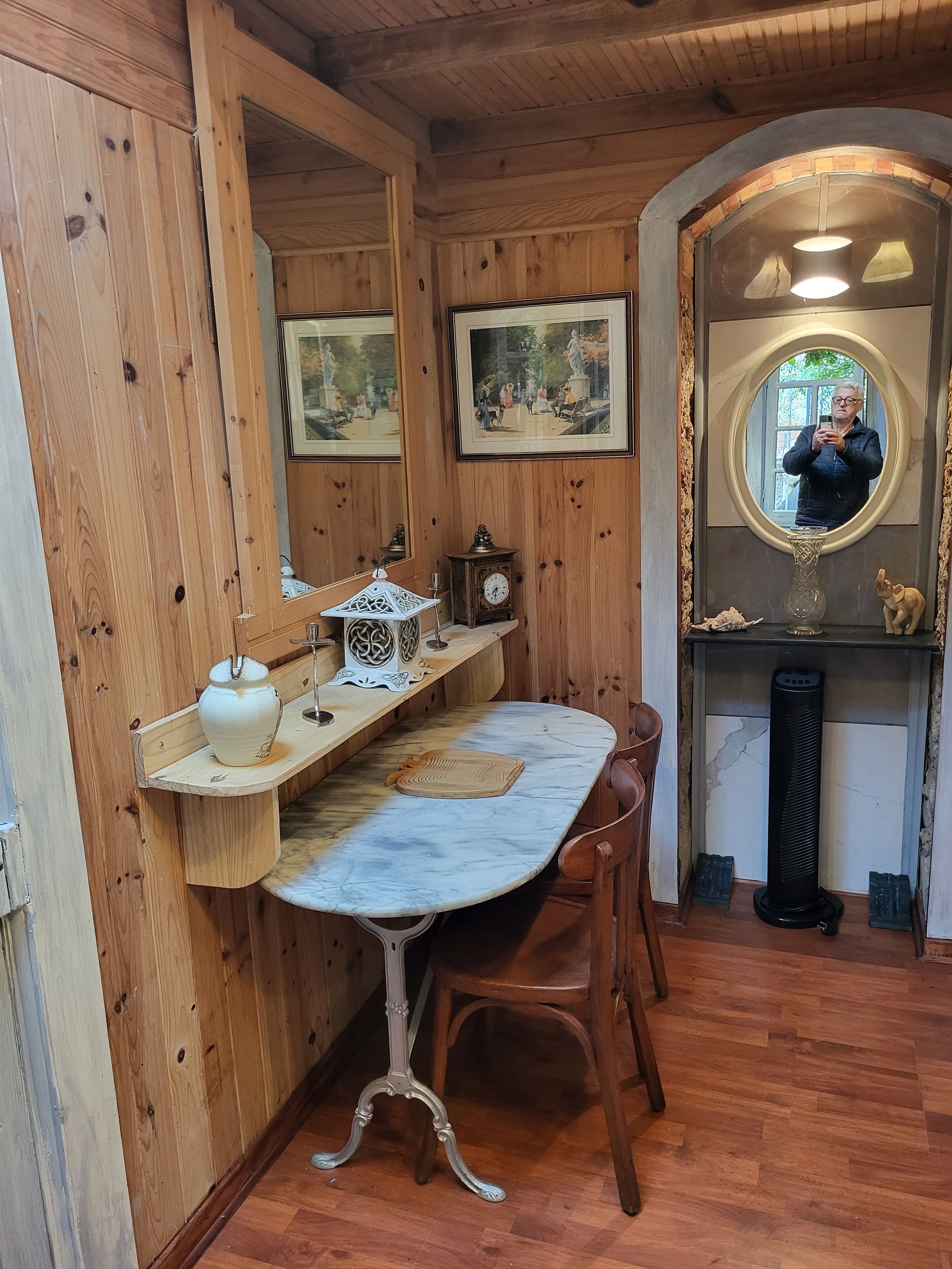 Une pièce en bois avec une table en marbre, des chaises en bois, une horloge, un vase et des tableaux encadrés accrochés au mur.