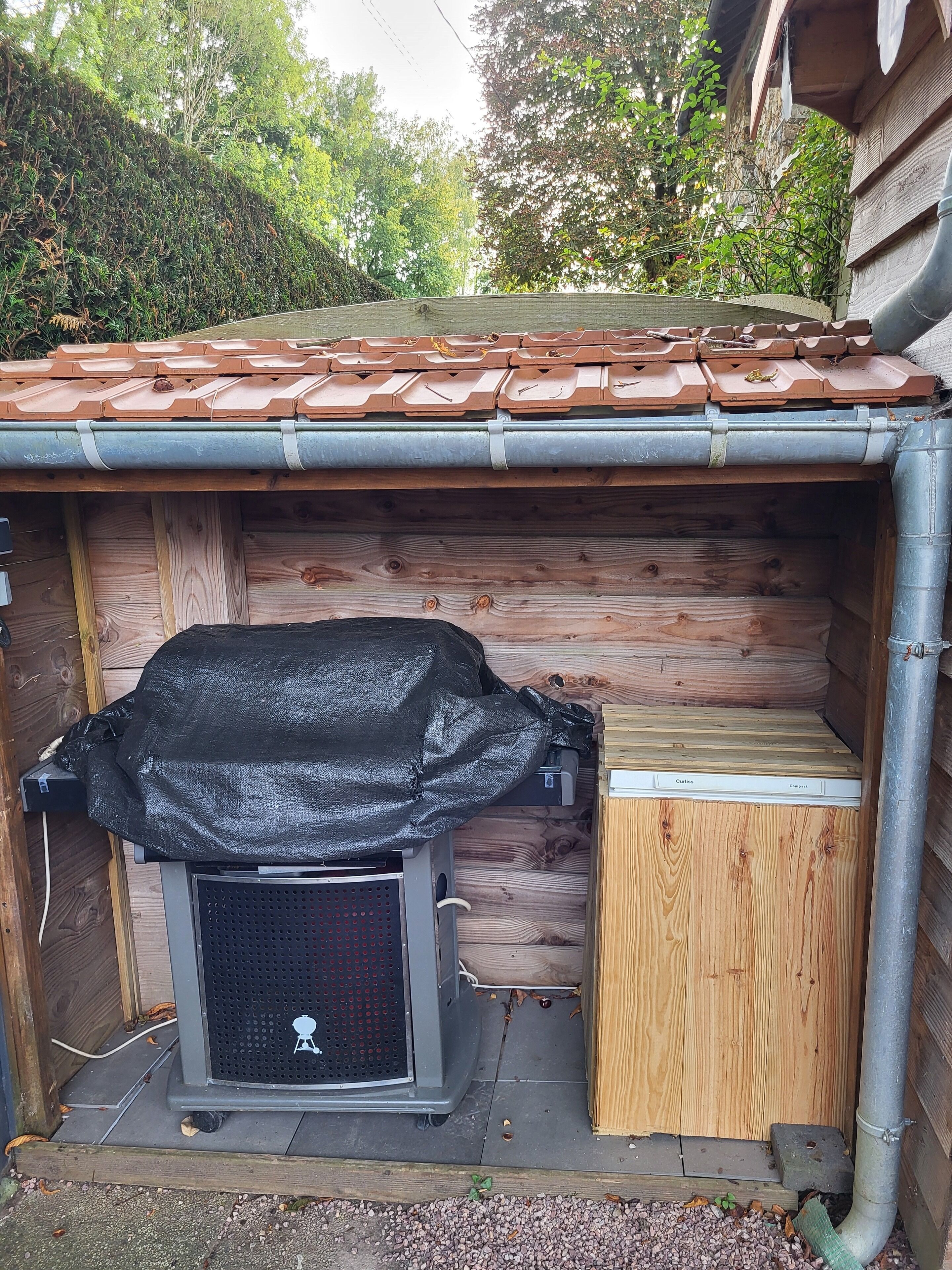 Une structure extérieure en bois, dotée d’un gril en métal, d’une petite armoire en bois et d’un tuyau en métal.