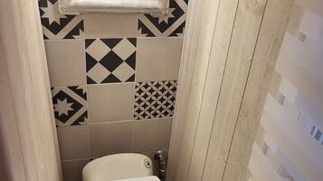 Ein kleines, schmales Badezimmer mit einer weißen Toilette, einem Fenster über dem Waschbecken und Wandfliesen mit Muster.