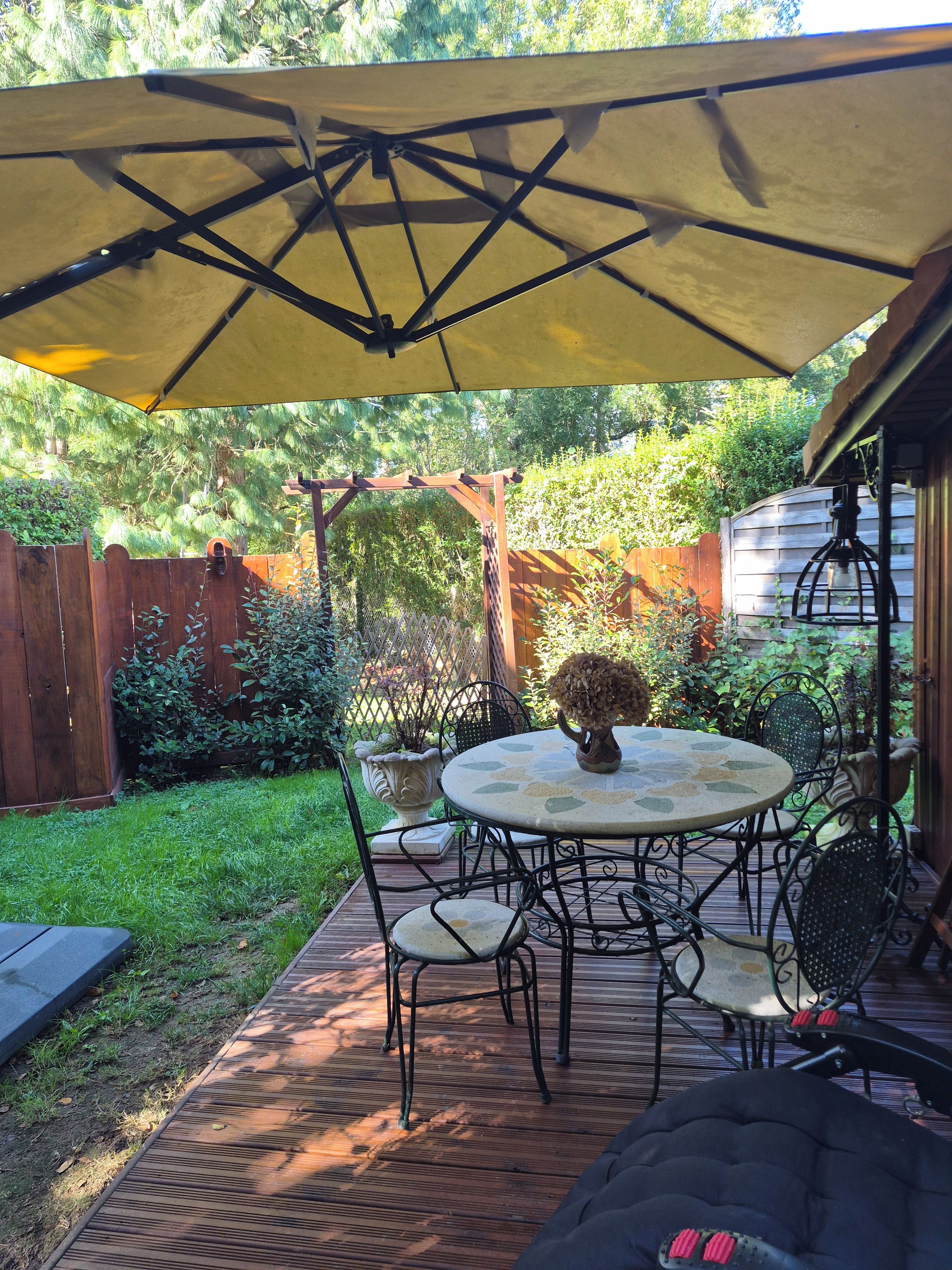 Eine Terrasse mit rundem Tisch und Stühlen, einem gelben Sonnenschirm und einem Holzdeck.
