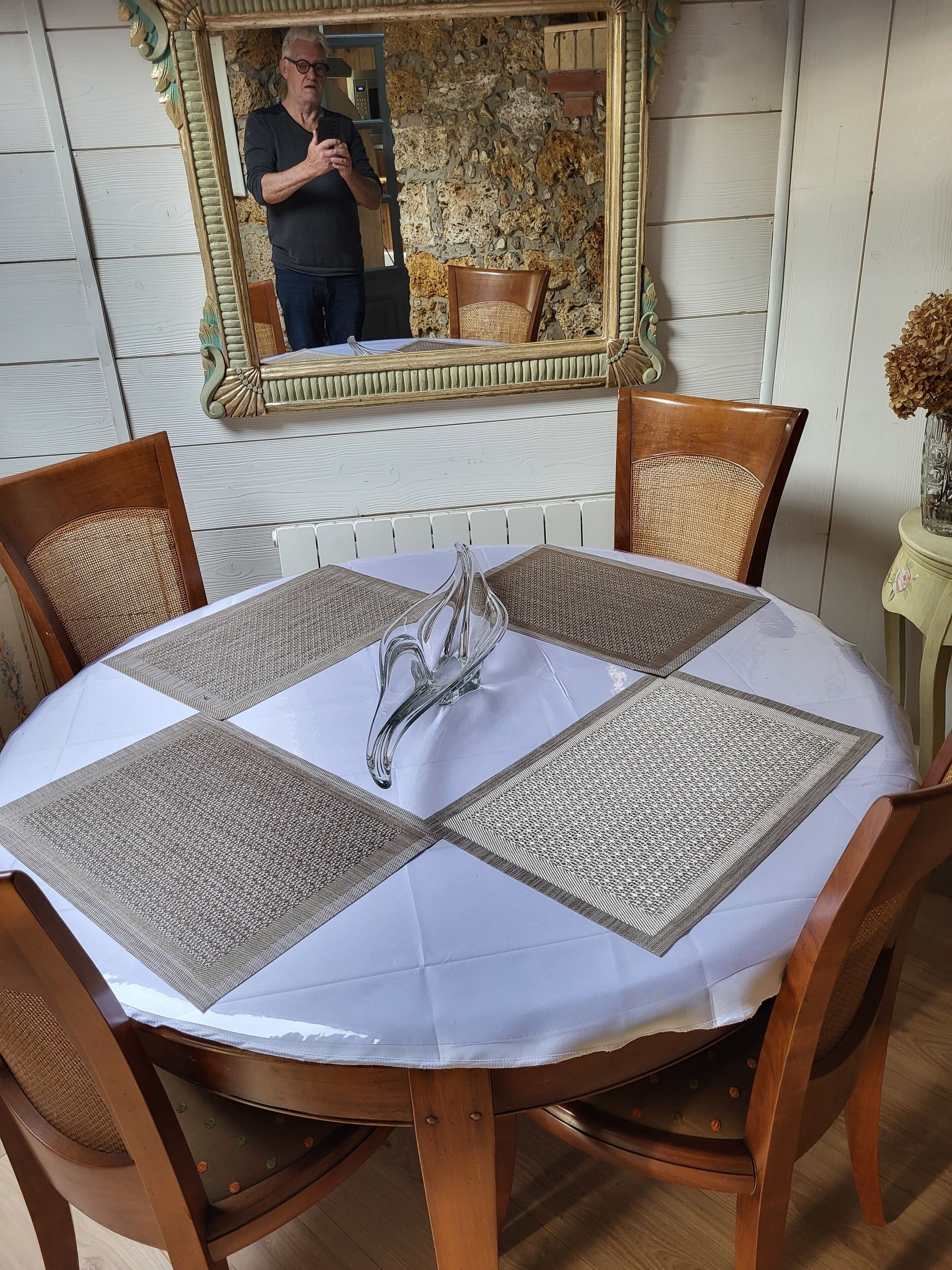 A round dining table with a white tablecloth and four woven placemats.