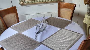 A round dining table with a white tablecloth and four woven placemats.