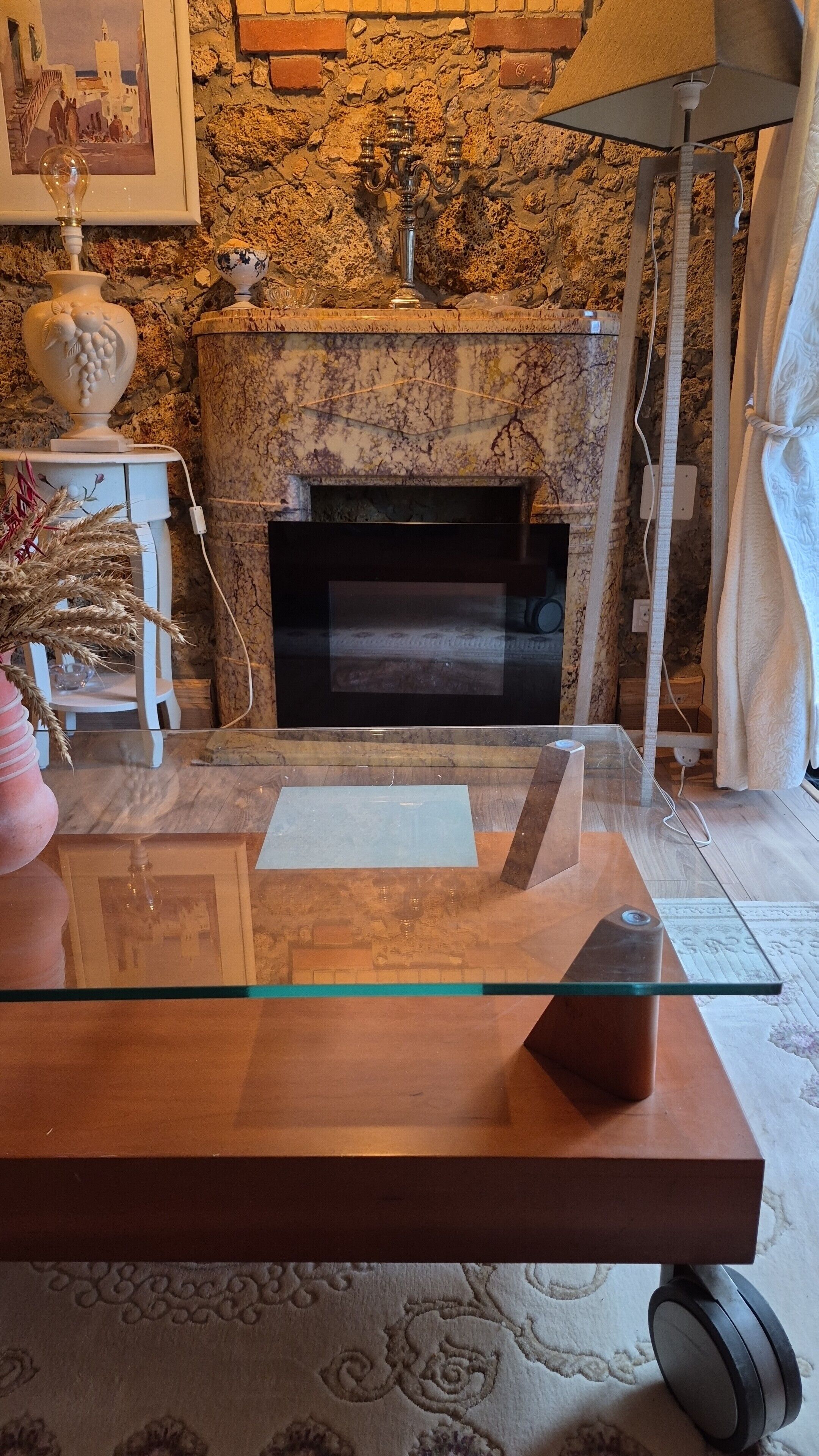 A room with a marble fireplace, a glass coffee table, and a framed picture on the wall.