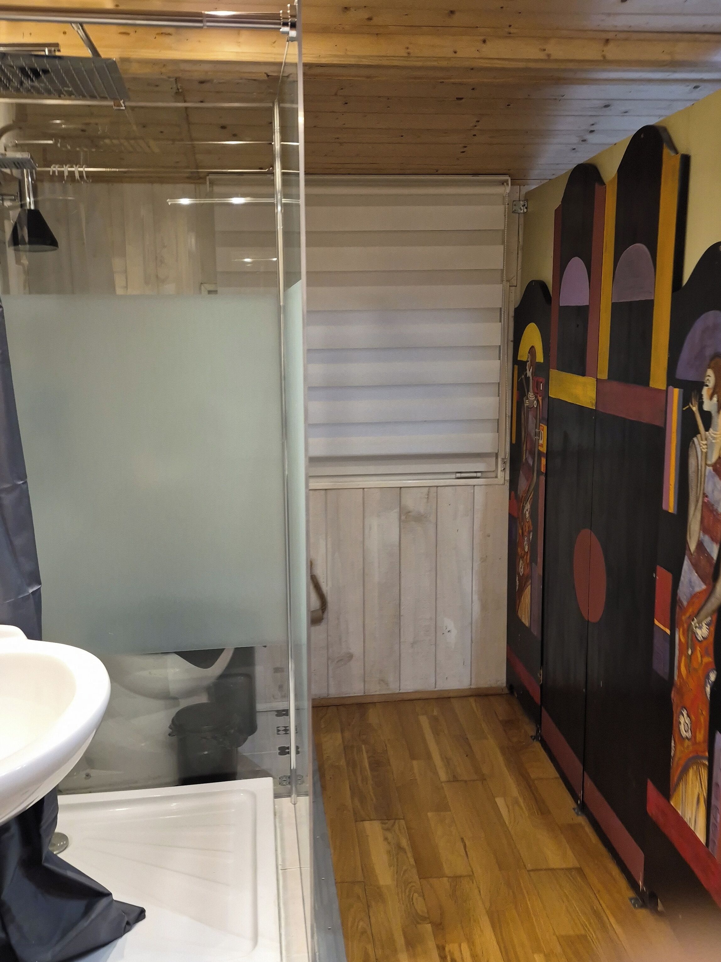 A bathroom with a glass shower enclosure, a white sink, and a wooden floor.