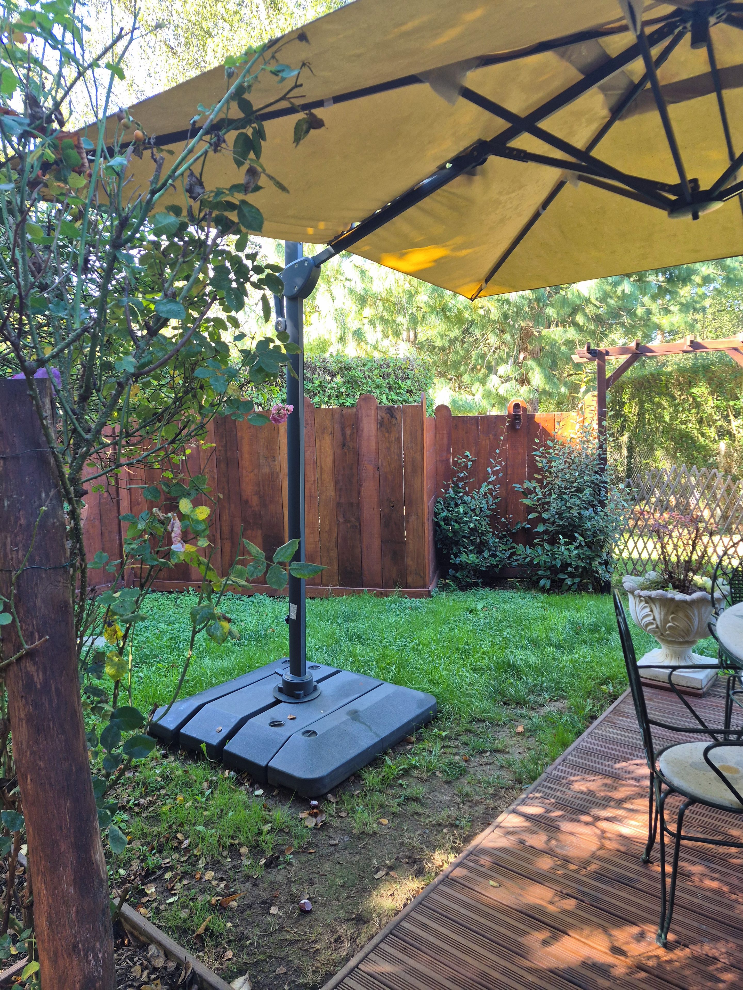 Un patio con mesa y sillas, un paraguas amarillo y una valla de madera al fondo.