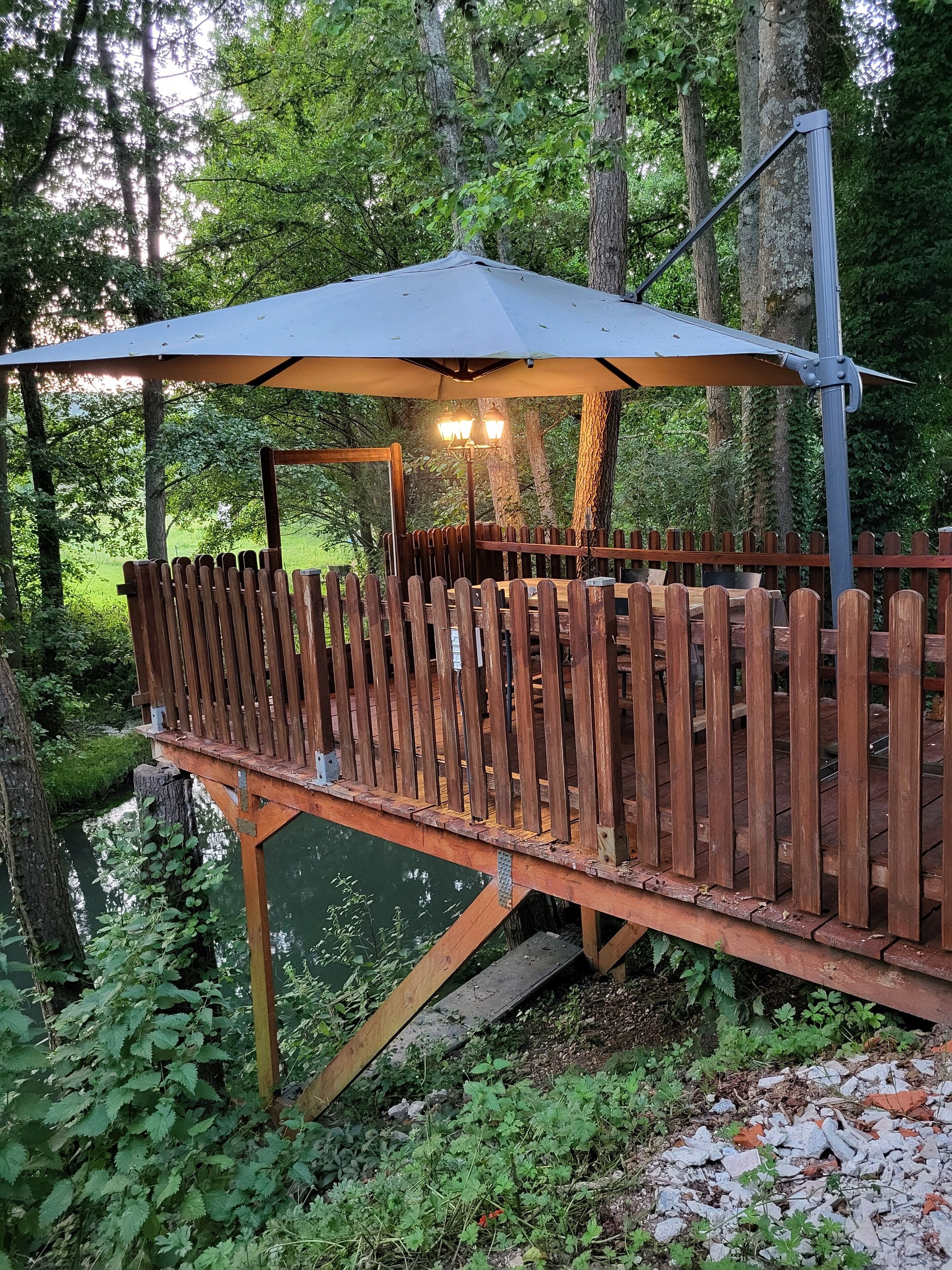 Eine Holzterrasse mit Baldachin und einer Lampe, die auf ein Gewässer blickt.