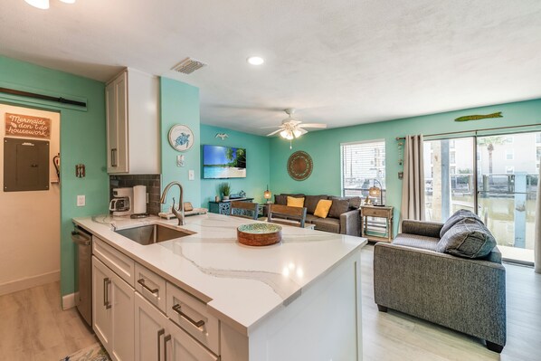 A modern kitchen with a large island, a dining area with a sofa, and a view of the outside. - First-Floor Waterfront Condo | Pool, Hot Tub & Canal Views (Corpus Christi)