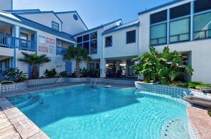A swimming pool with a blue and white tiled edge, surrounded by a wooden deck. - First-Floor Waterfront Condo | Pool, Hot Tub & Canal Views (Corpus Christi)