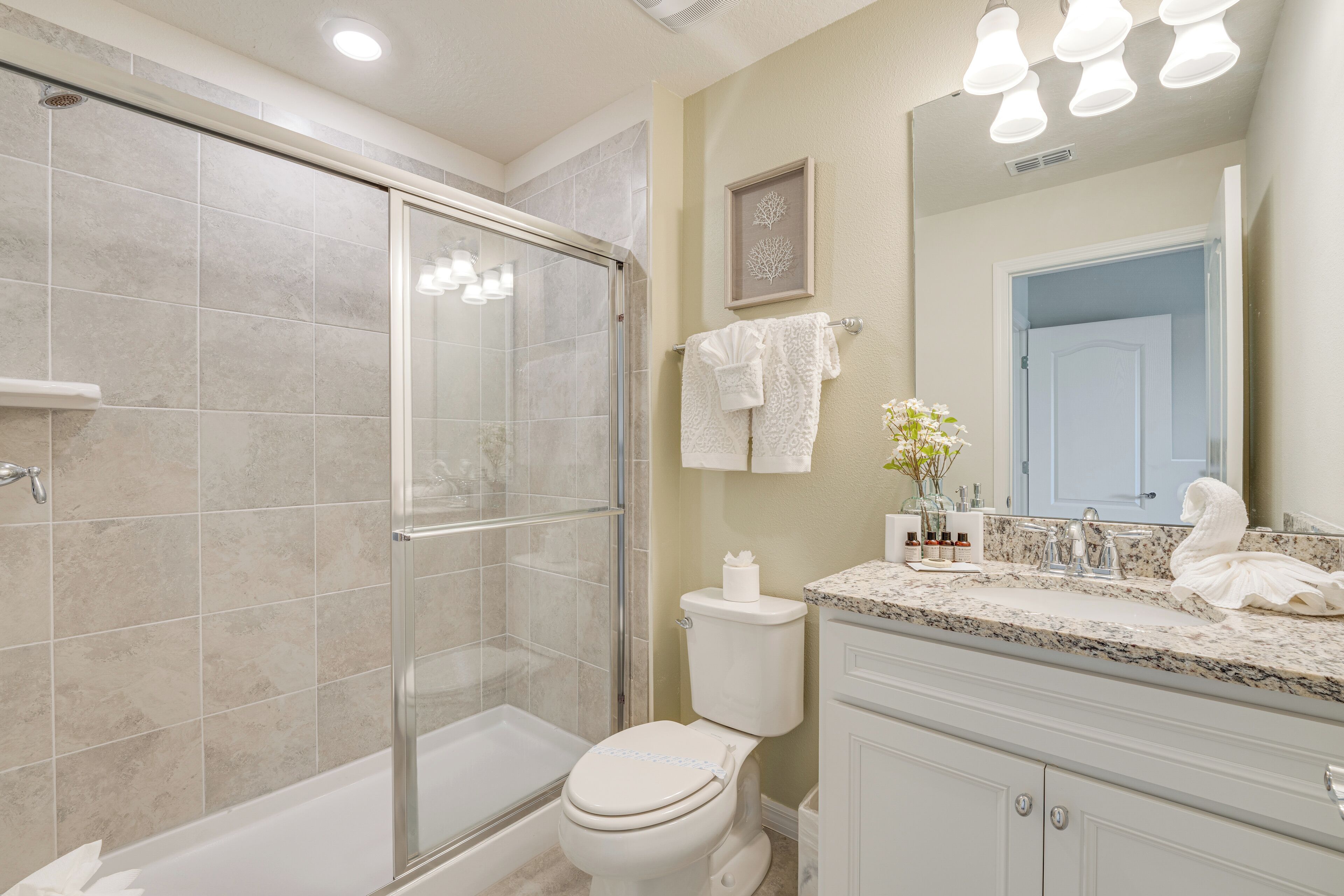 A modern bathroom with a glass-enclosed shower, a white toilet, a vanity with a sink, and a mirror.