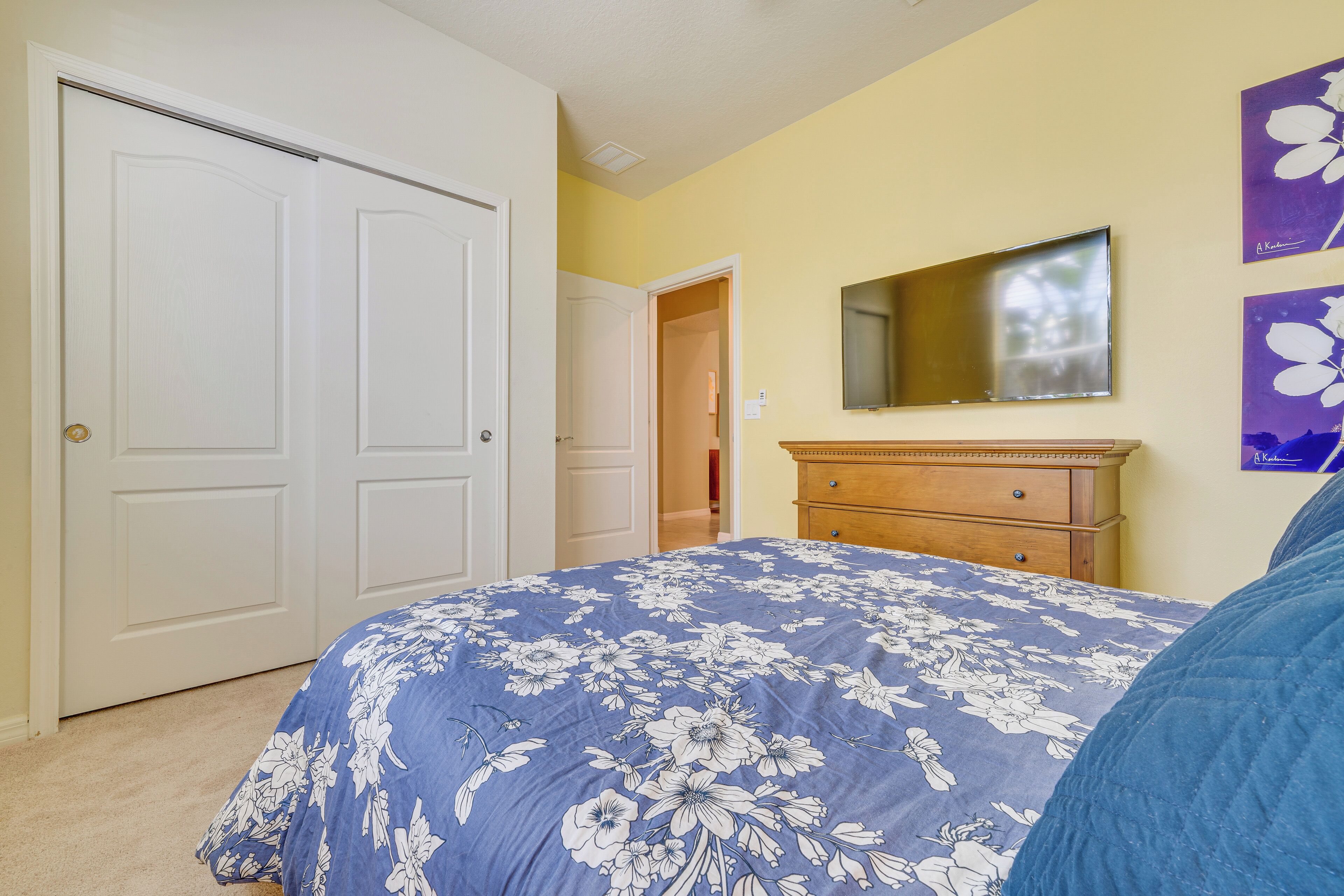 Une chambre avec une porte à deux battants, un lit recouvert d’une couvre-lit à motifs floraux, une commode et un miroir au mur.