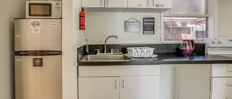 A kitchen with white cabinets, a microwave, a sink, and a window with blinds.