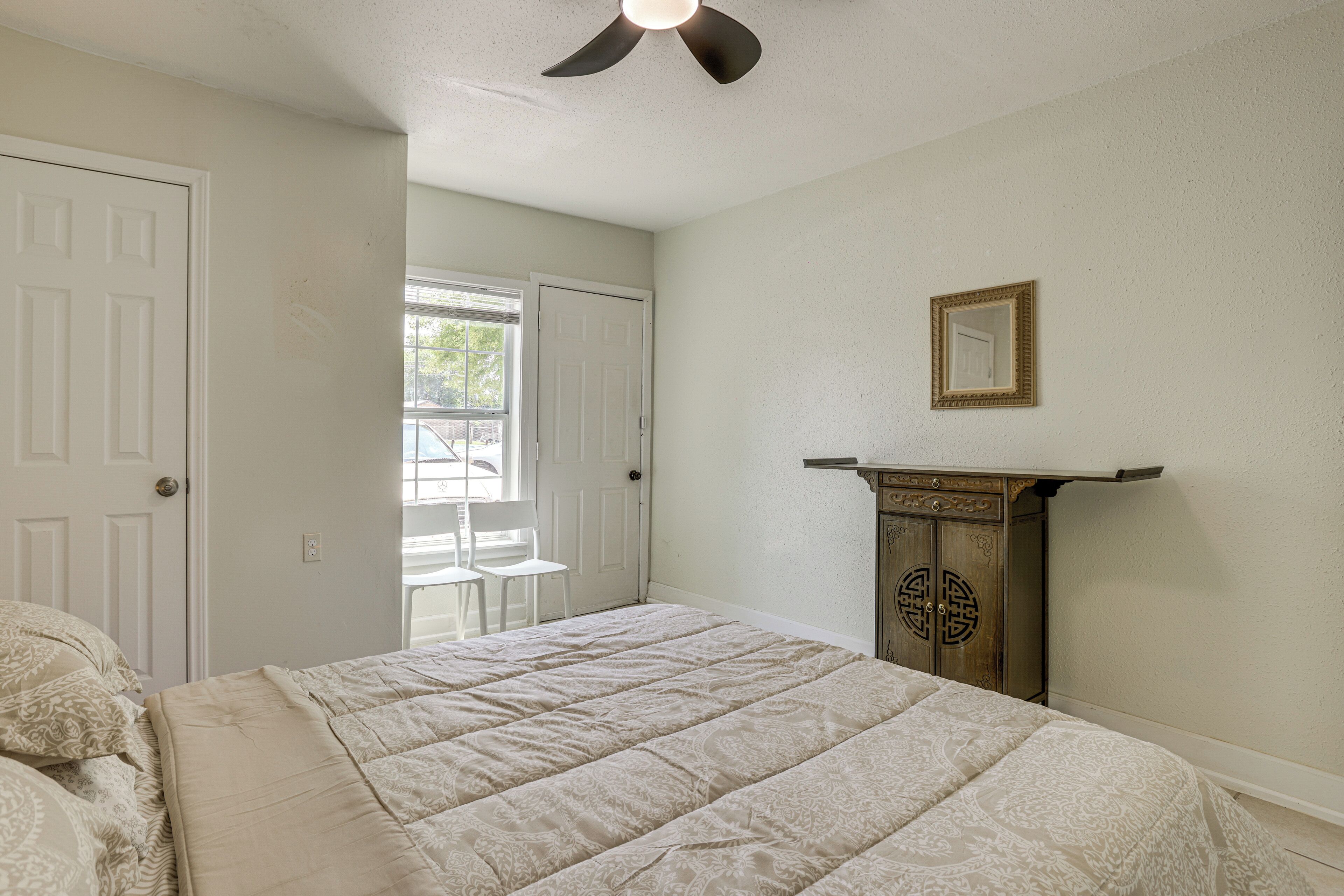 A bedroom with a bed, a ceiling fan, a door, and a window.