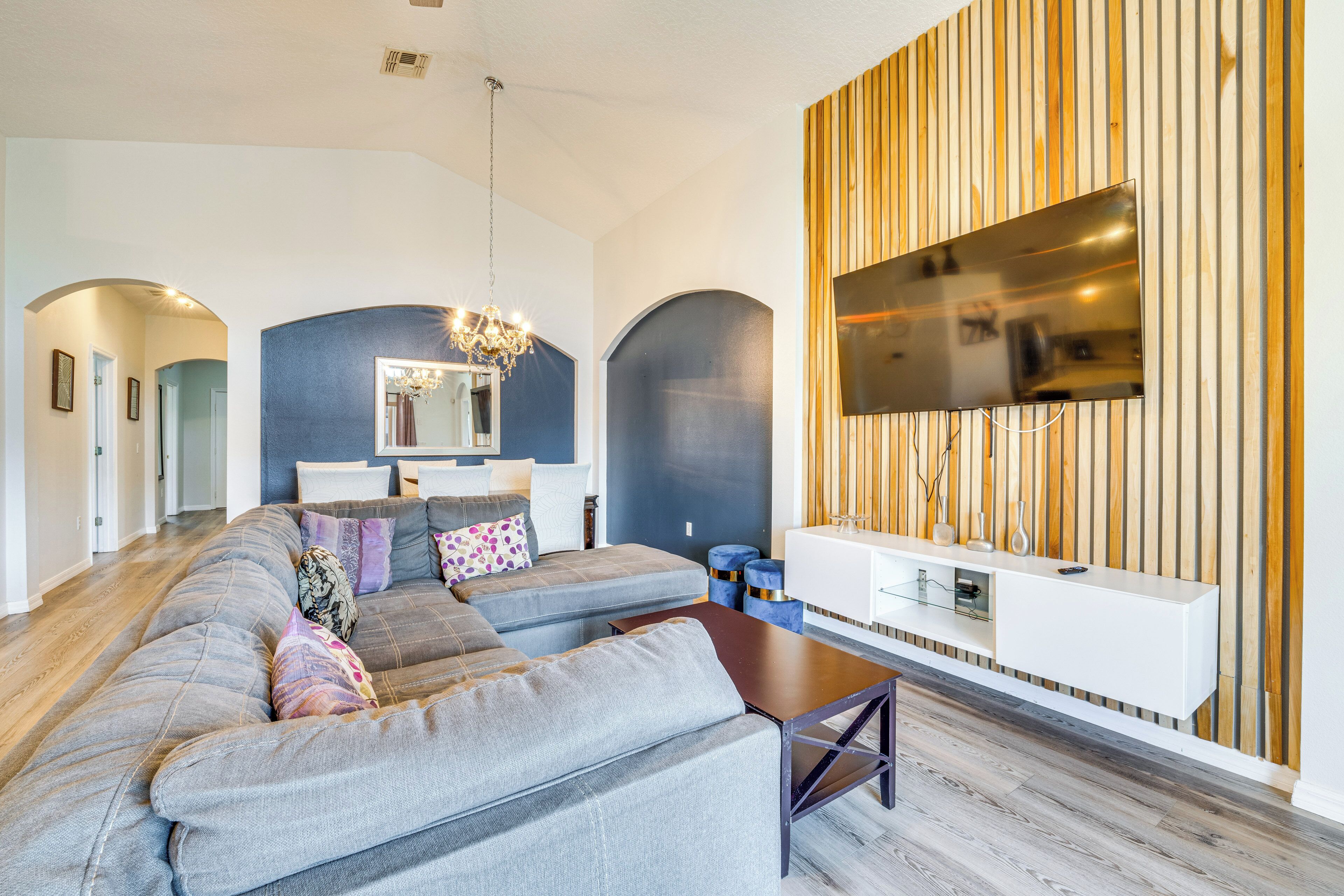 Un salon moderne avec un canapé d’angle, un mur d’accent en bois, un téléviseur à écran plat et un lustre.