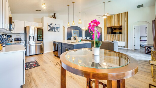 A modern kitchen with stainless steel appliances, a dining area with a glass table, and a living space with a TV and wooden paneling. - 10 Mi to Disney: Family Retreat w/ Game Room! (Davenport)
