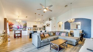 A spacious living room with a grey sectional sofa, a coffee table, and a dining area with a chandelier. - 10 Mi to Disney: Family Retreat w/ Game Room! (Davenport)