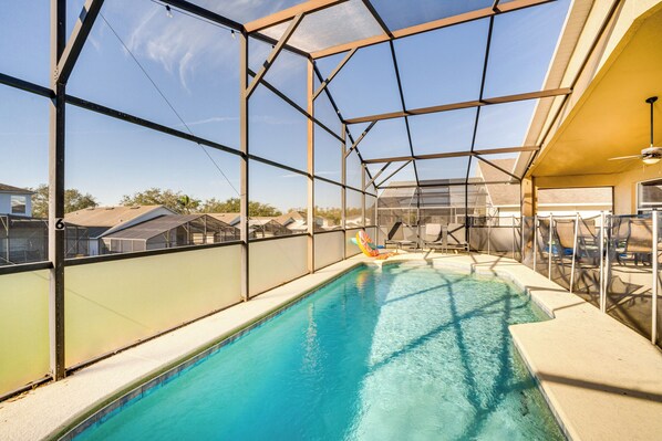 An indoor swimming pool with clear glass walls, a ceiling fan, and a view of the surrounding neighborhood.