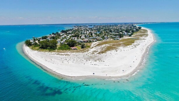 An aerial view of a coastal resort with a long sandy beach, clear turquoise waters, and a dense cluster of buildings. - LBK Whitney Beach Retreat 1 (Longboat Key)