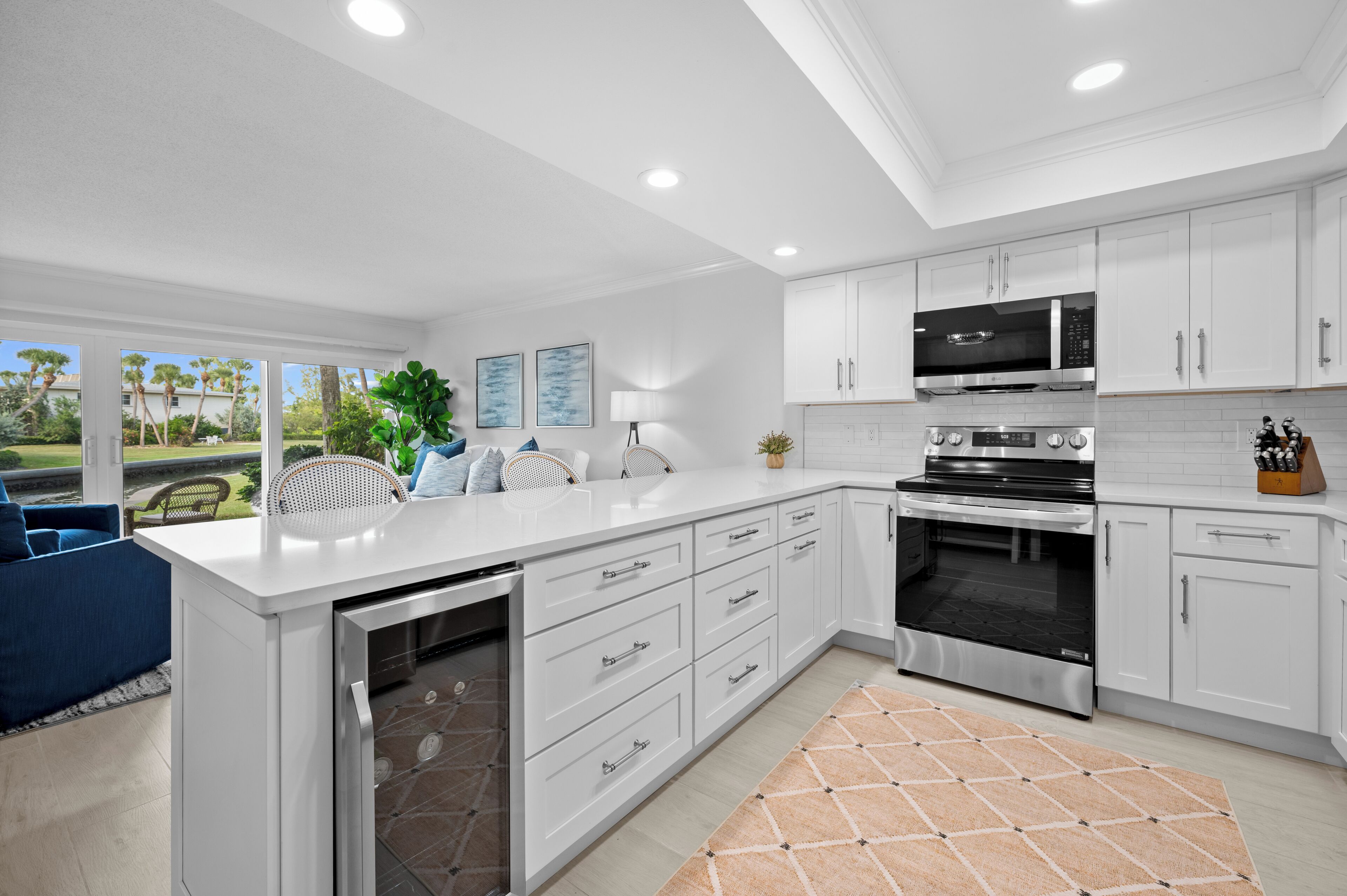 Una cocina moderna con armarios blancos, un microondas integrado y un horno. Hay un comedor con una silla azul y una planta en la encimera.