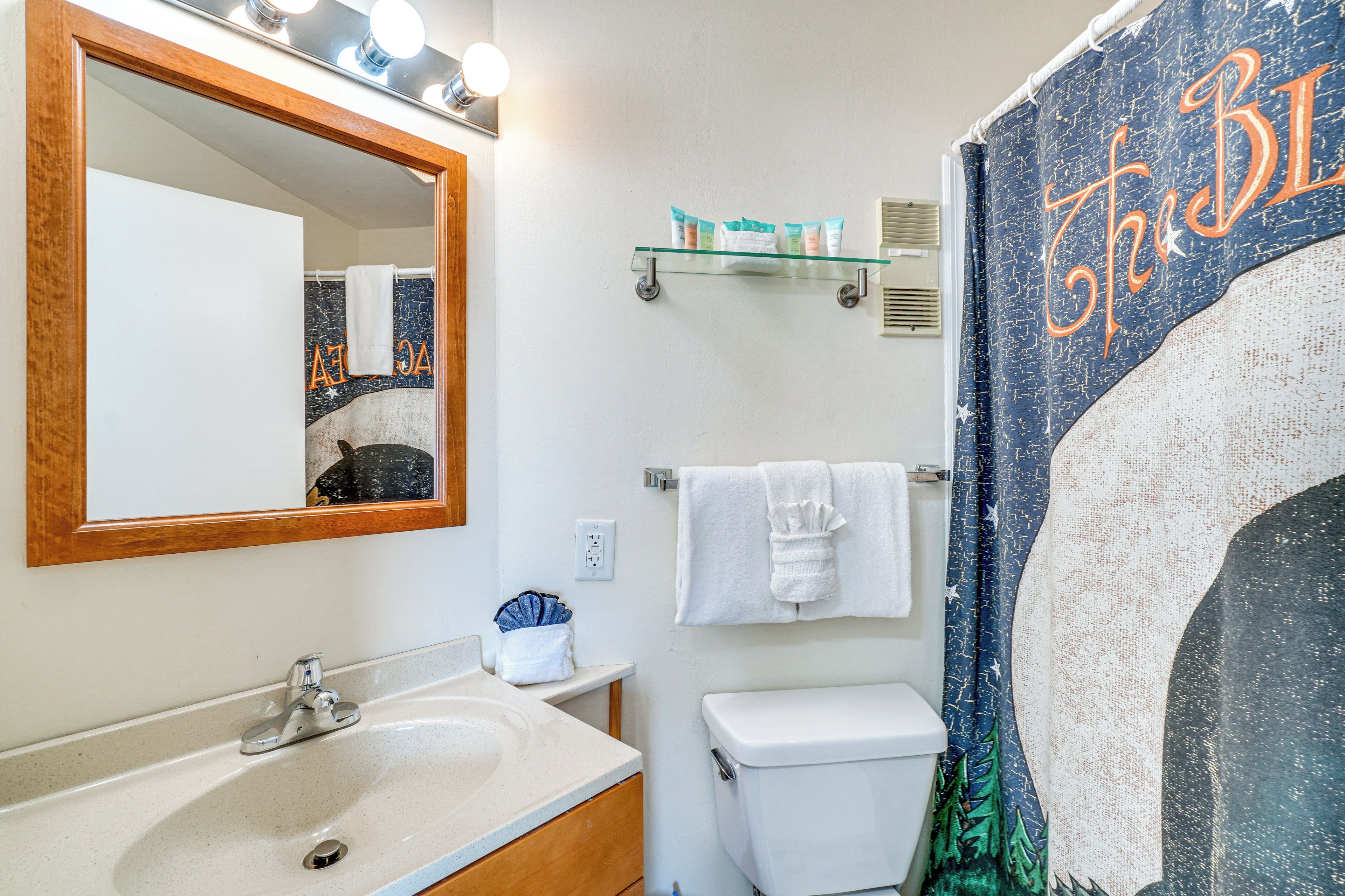 A bathroom with a sink, mirror, toilet, and a shower curtain with a large moon design.