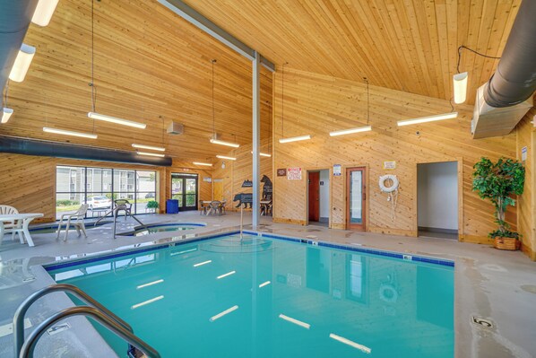 Una piscina interior con paredes y techo de madera, rodeada de sillones y mesas.
