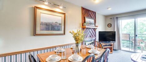 A dining area with a wooden table set for four, a vase with flowers, and a television in the background.