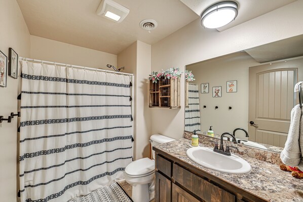 A bathroom with a shower curtain, toilet, sink, and mirror. - Walk to Downtown: Family-friendly Cody Home! (Cody)
