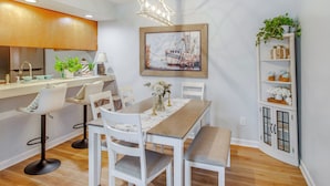 A modern kitchen with white cabinetry, a dining table with chairs, a pendant light, and a painting of a ship on the wall. - 1/2 Mi to Shore: Condo w/ Balcony in Myrtle Beach! (Myrtle Beach)