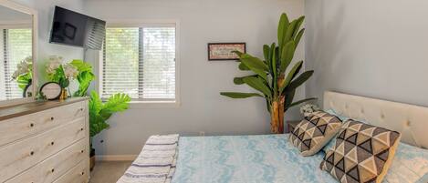A bedroom with a bed, dresser, TV, and large plant.